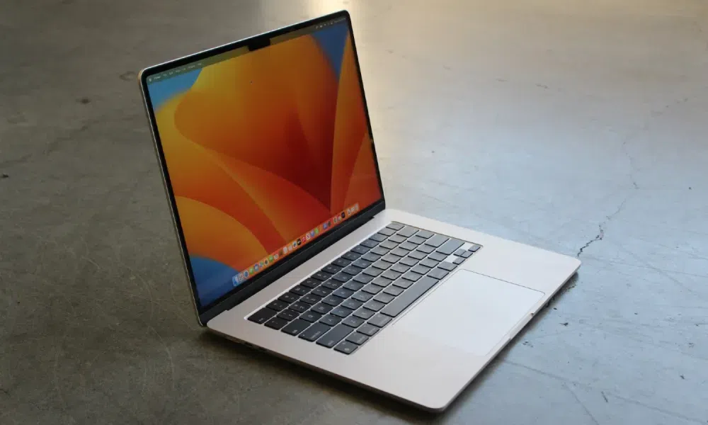 A MacBook Pro with a vibrant orange and blue wallpaper on the screen, placed on a concrete floor with soft lighting reflecting off the surface.